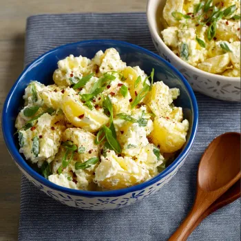 A bowl of potato salad with green onions and red peppers.