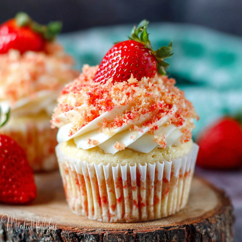 Two cupcakes with strawberries on top.