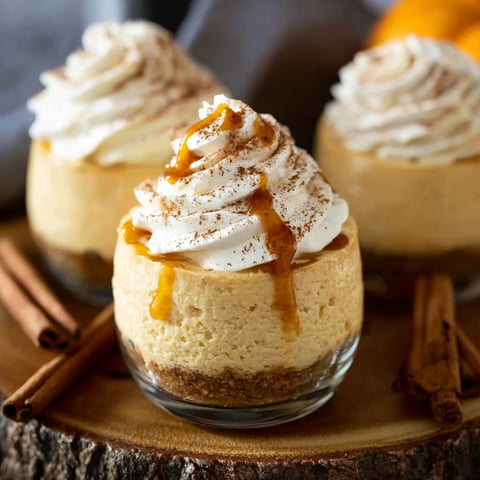 Two small pumpkin cheesecakes with whipped cream toppings.