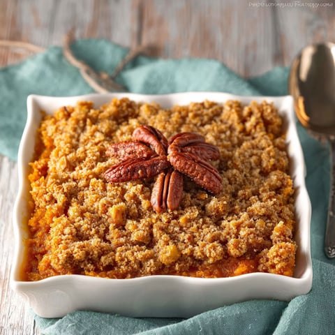 A white bowl filled with a sweet potato casserole with a pecan topping.