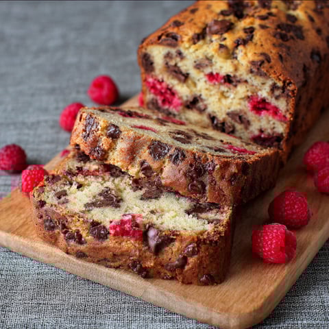 A slice of dark chocolate banana bread with raspberries on top.