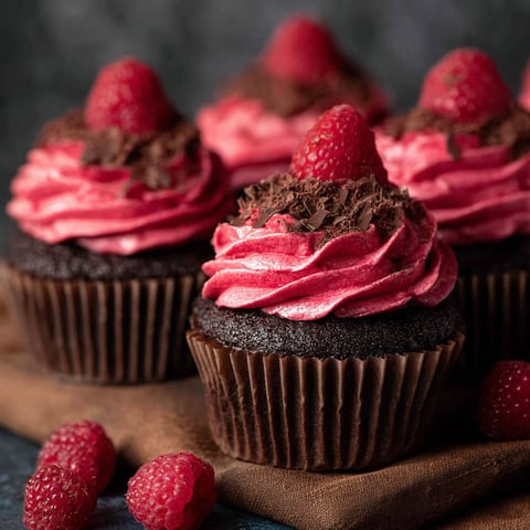 Three chocolate raspberry cupcakes with strawberries on top.